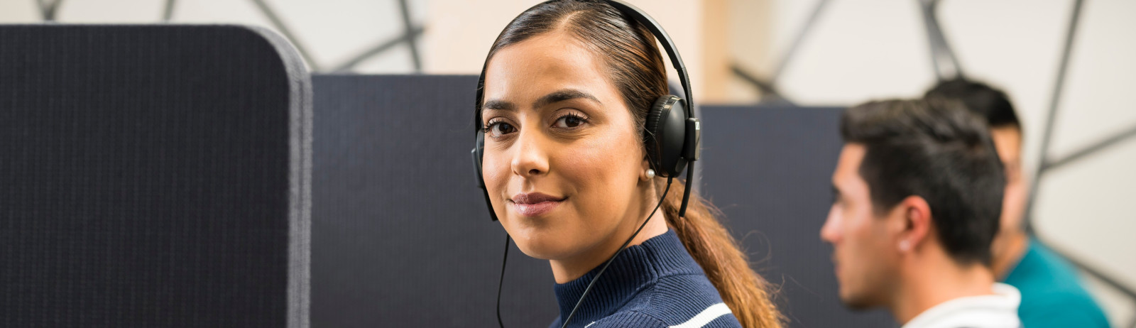 Female IELTS test taker wearing a blue turtleneck top listening to an audio clip during an IELTS on computer session