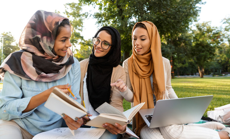 Three female IELTS test takers wearing hijabs prepare for IELTS in a park