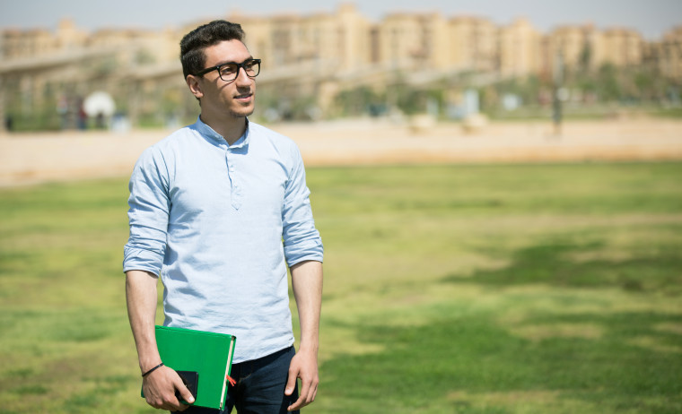 Male test taker in a wearing a blue shirt and spectacles holding a book in a park