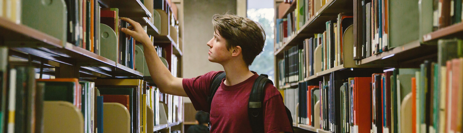 A male test taker looking at the book in a library bookshelf.