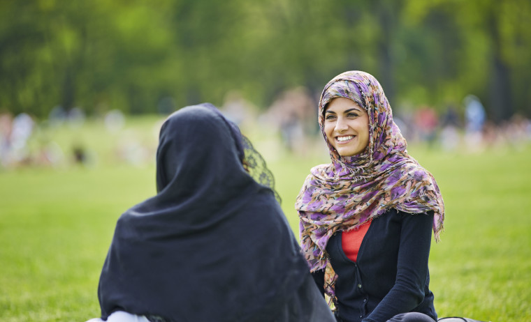 Two female test takers wearing a headscarf and having a happy conversation with each other in a park.