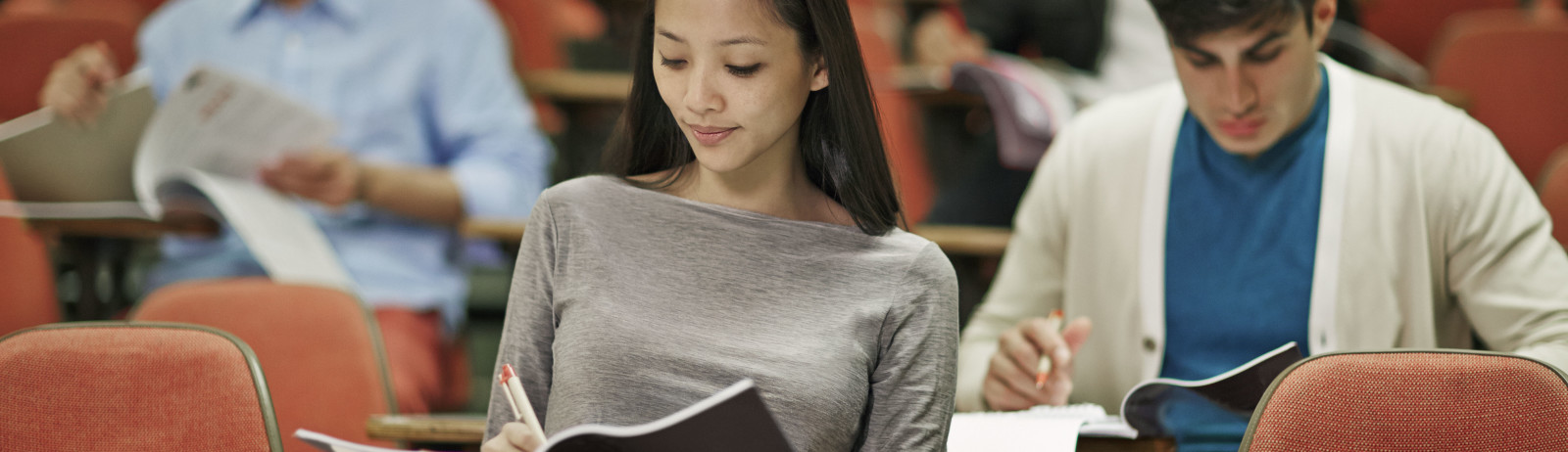 Female IELTS test taker wearing a grey full-sleeved t-shirt prepares for IELTS Writing along with other test takers.