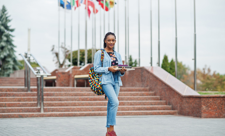 A female student wearing a denim shirt stands with her backpack on.