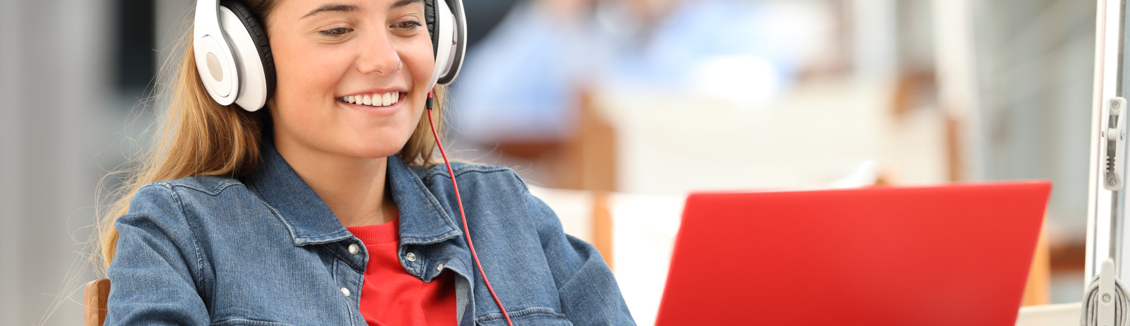 Female IELTS test taker wearing a blue denim jacket and a headphone, prepares for computer-delivered IELTS in her laptop.
