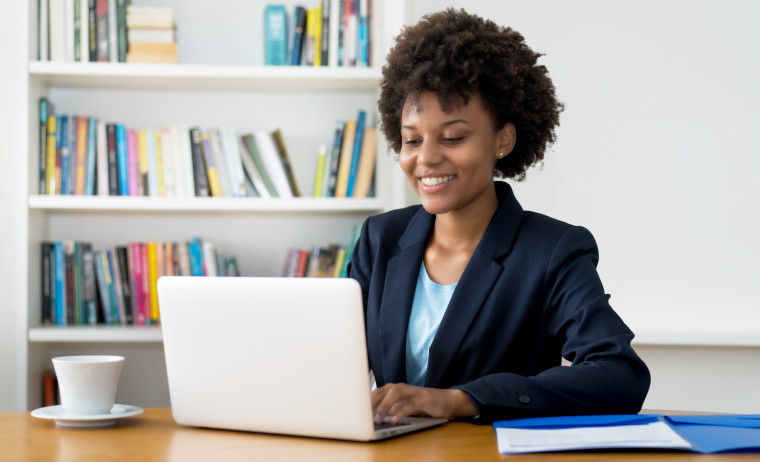 A female professional wearing a navy blue blazer looks at something on her laptop