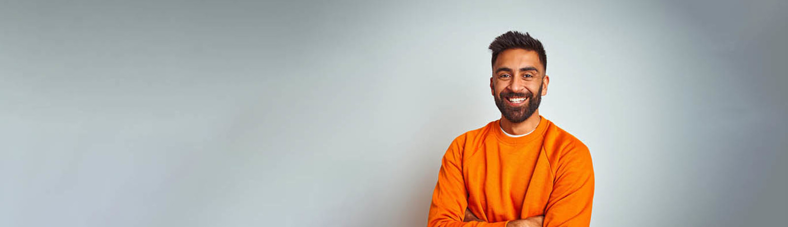 Young man wearing orange sweater over isolated white background happy face smiling with crossed arms looking at the camera.