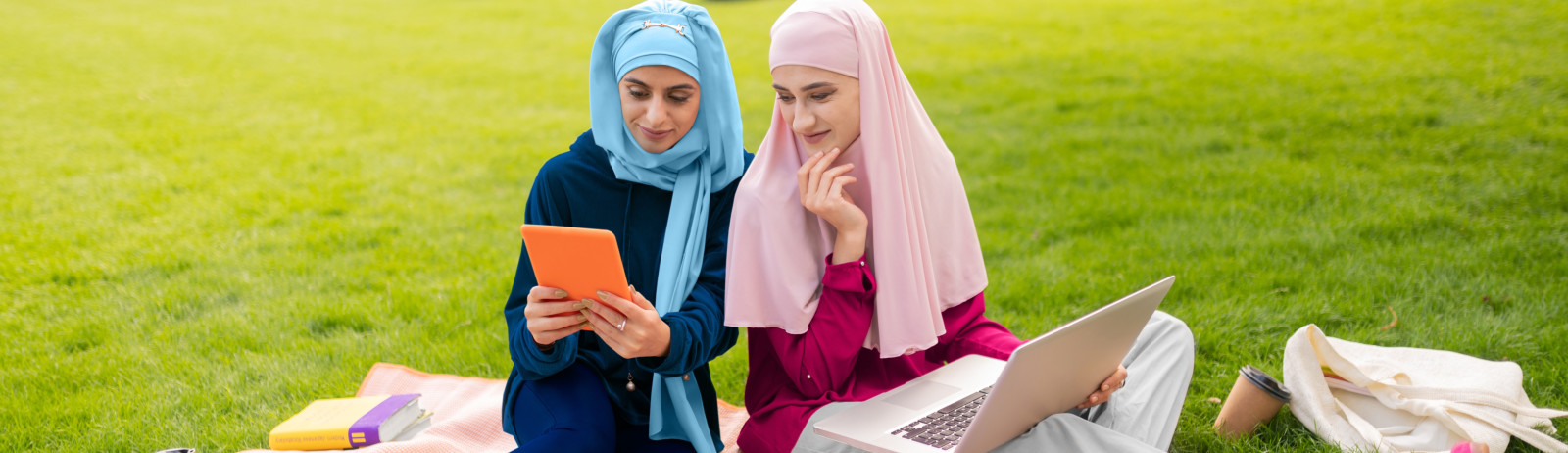 Two female IELTS test takers wearing hijab sits on the lawn and prepares for IELTS - Middle East