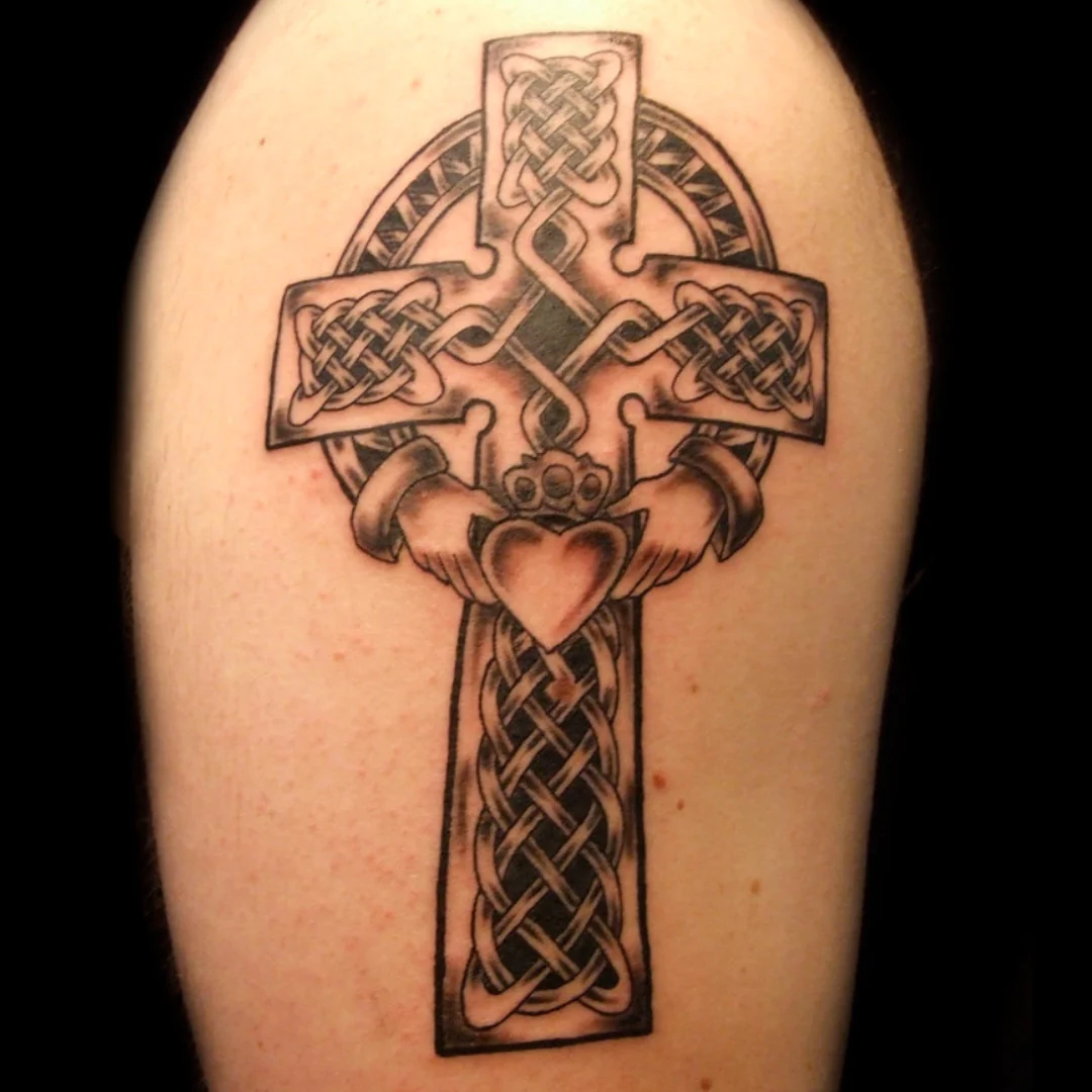 A large, weathered stone Celtic cross standing proudly atop a lush green  hill, its four arms