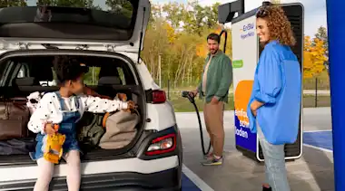 Familie lädt E-Auto, im Kofferraum sitzt ein Kind