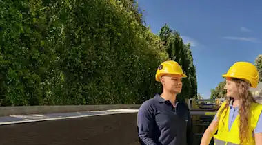 Mann und Frau mit Helmen vor Baugrube