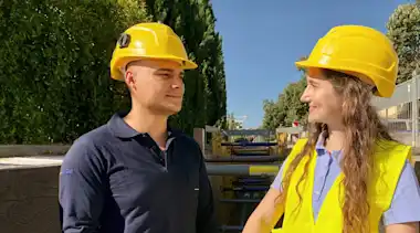 Mann und Frau mit Bauhelmen vor Hecke blauer Himmel