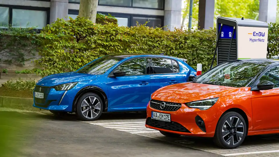 Zwei Elektroautos (Opel und Peugeot) an einer Ladesäule.