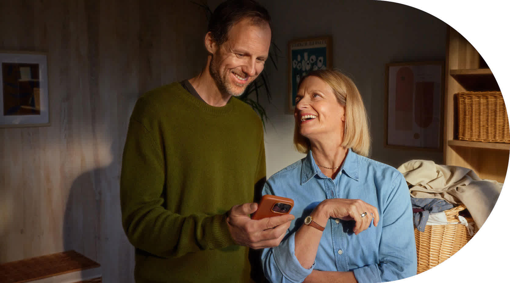 Eine Ehepaar steht in der Waschküche und schaut lächelnd auf ein Smartphone.