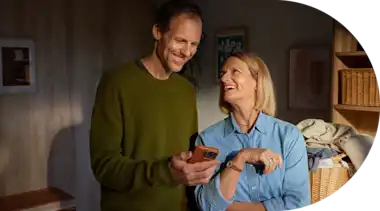 Eine Ehepaar steht in der Waschküche und schaut lächelnd auf ein Smartphone.