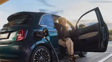 Eine junge Frau lädt während des Sonnenuntergangs ihr Elektroauto an einer EnBW Ladesäule.