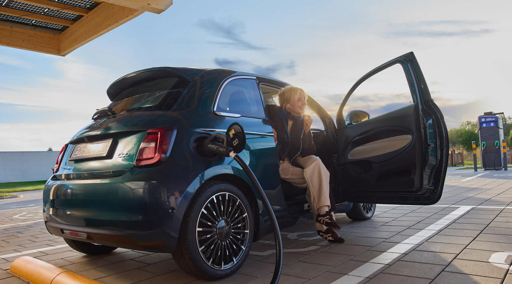 Eine junge Frau lädt während des Sonnenuntergangs ihr Elektroauto an einer EnBW Ladesäule.