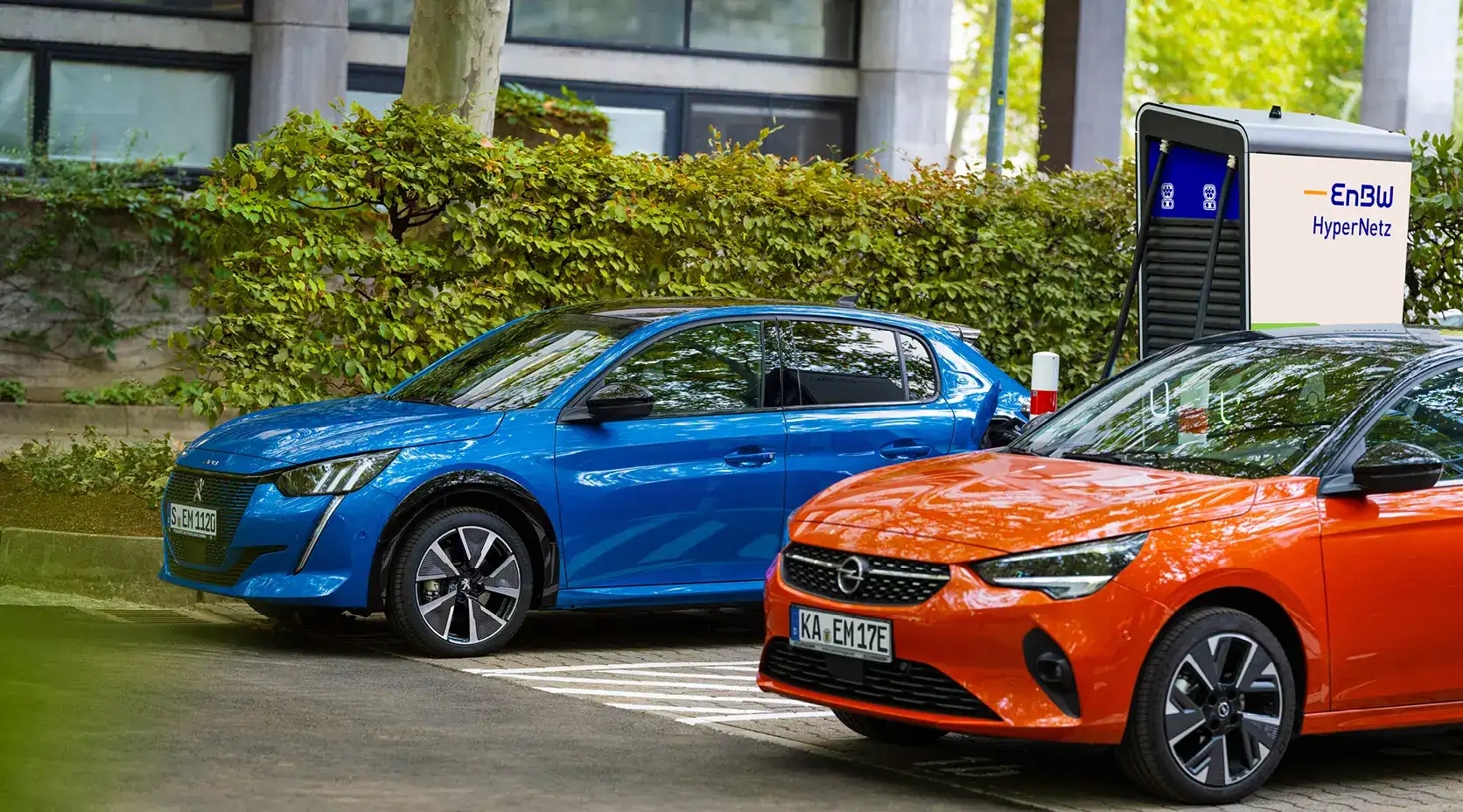 Zwei Elektroautos (Opel und Peugeot) an einer Ladesäule.