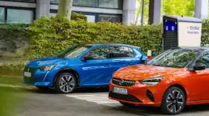 Zwei Elektroautos (Opel und Peugeot) an einer Ladesäule.
