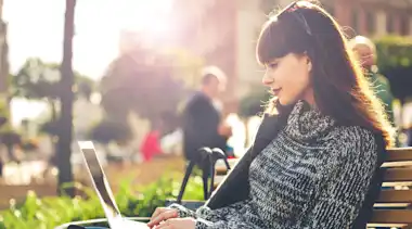 Frau sitzt mit Notebook auf einer Parkbank