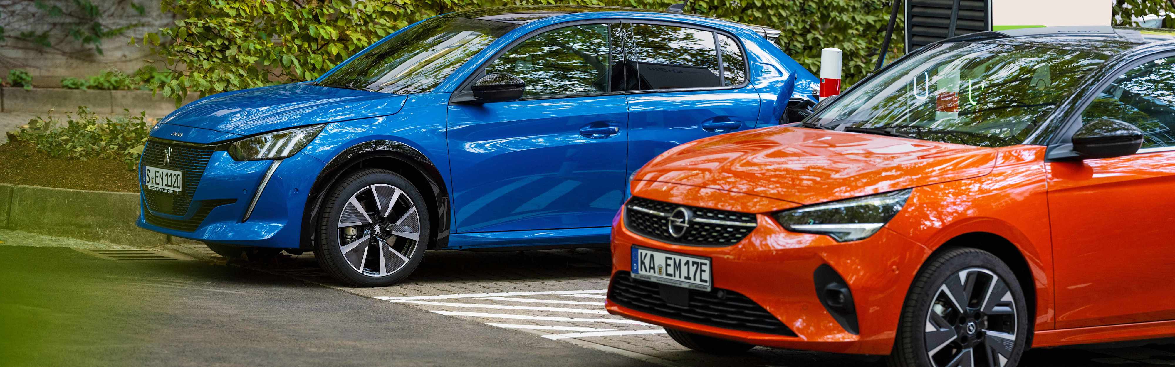Zwei Elektroautos (Opel und Peugeot) an einer Ladesäule.