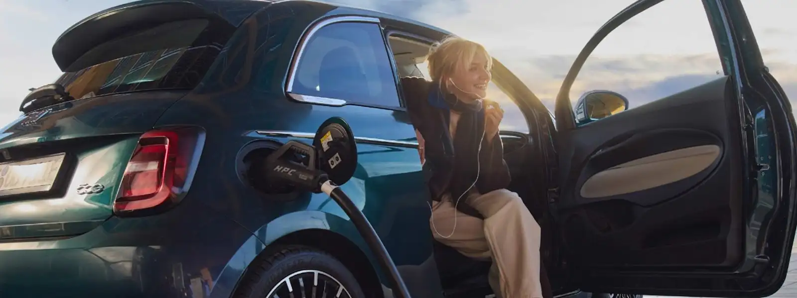 Eine junge Frau lädt während des Sonnenuntergangs ihr Elektroauto an einer EnBW Ladesäule.