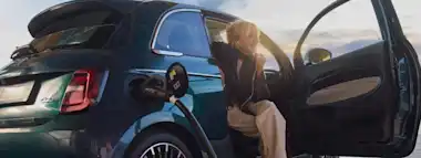 Eine junge Frau lädt während des Sonnenuntergangs ihr Elektroauto an einer EnBW Ladesäule.