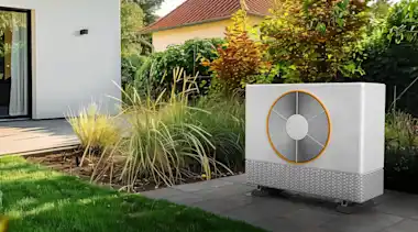 Weiße Wärmepumpe auf grüner Wiese vor Terrasse