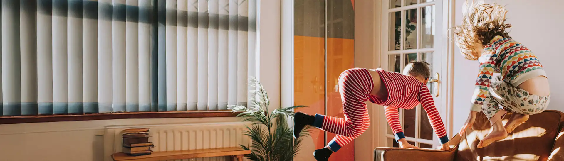Zwei Kinder hüpfen vom Sofa im Wohnzimmer