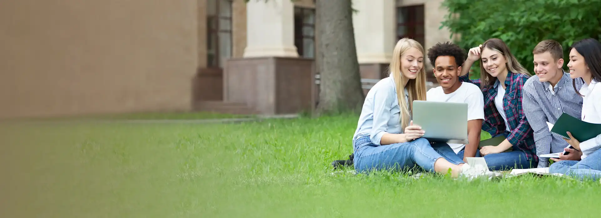 Studenten sitzen vor dem Campus auf der Wiese