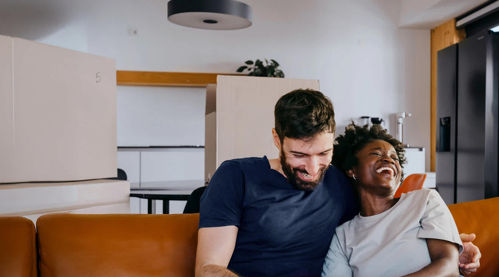 Ein junges Pärchen sitzt lachend auf der Couch und schaut auf ein Smartphone.