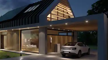 Einfamilienhaus bei Nacht mit ladendem Elektro-Fahrzeug im Carport