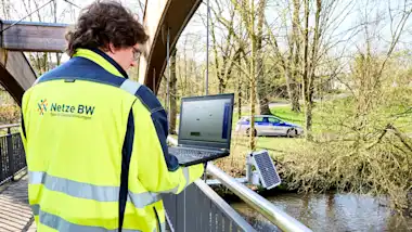Mann mit Laptop auf einer Brücke über einem Fluss