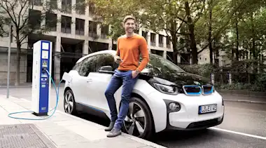 Junger Mann lehnt während des Ladevorgangs an BMW i3.