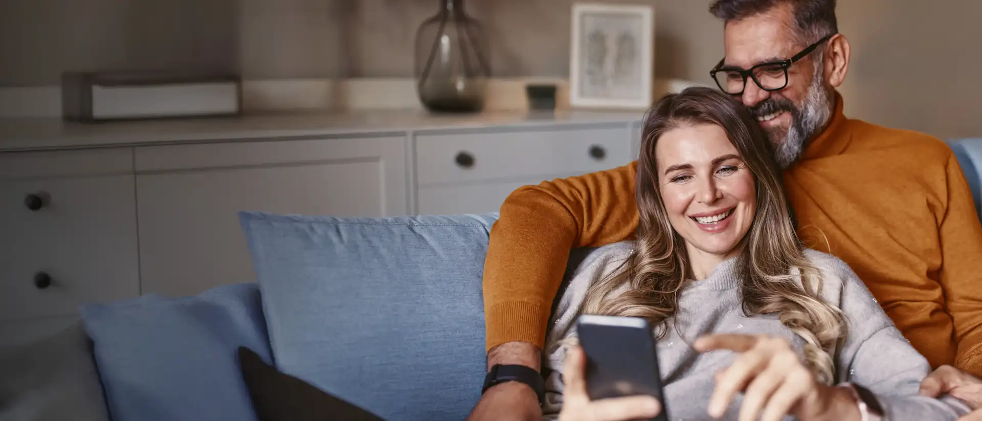Pärchen sitzt gemütlich auf der Couch und schaut auf ein Smartphone.