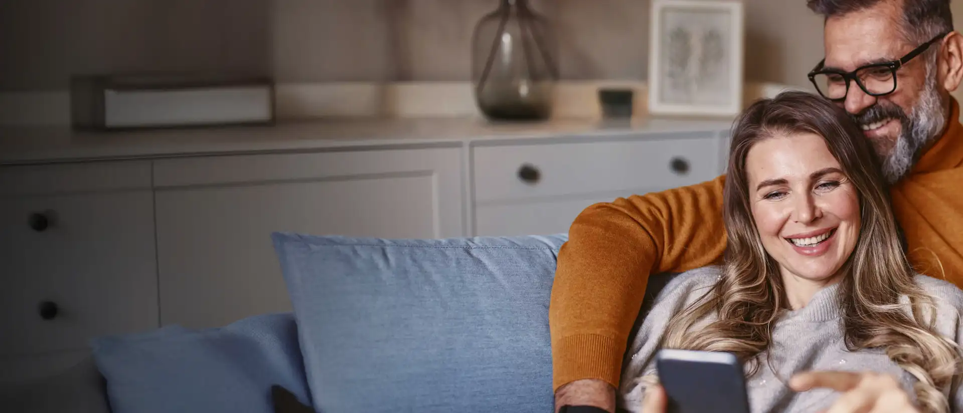 Pärchen sitzt gemütlich auf der Couch und schaut auf ein Smartphone.