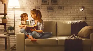 Mutter und Kind lesen auf dem Sofa ein Buch.