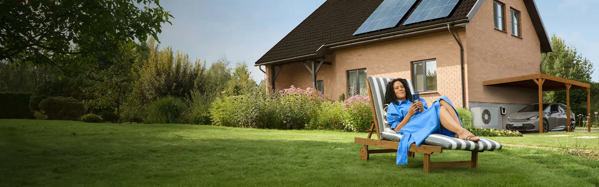 Eine Frau liegt entspannt auf einem Liegestuhl im Garten ihres Hauses.