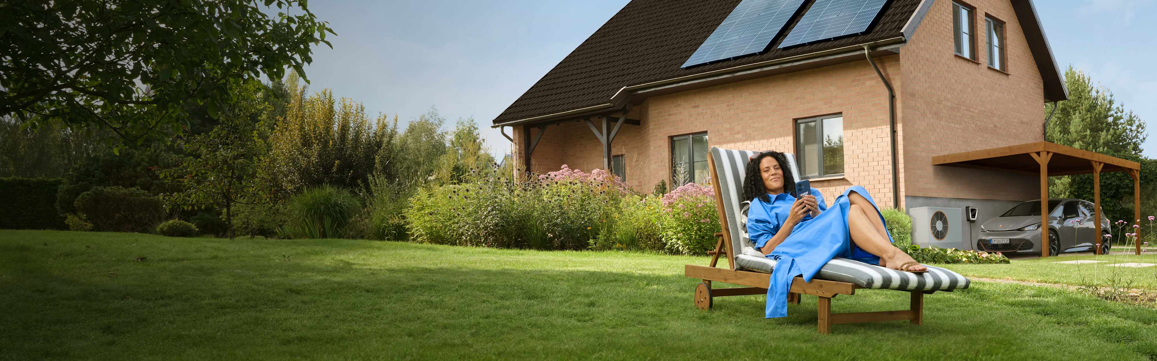 Eine Frau liegt entspannt auf einem Liegestuhl im Garten ihres Hauses.