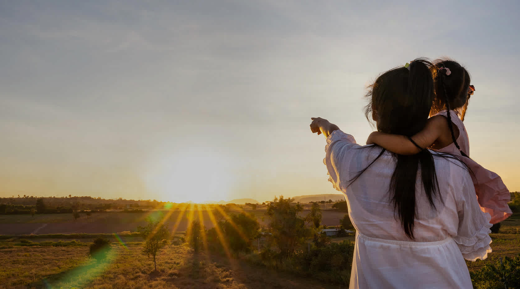 Frau mit Kind im Arm zeigt und blickt in Richtung aufgehende Sonne