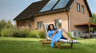 Eine Frau liegt entspannt auf einem Liegestuhl im Garten ihres Hauses.