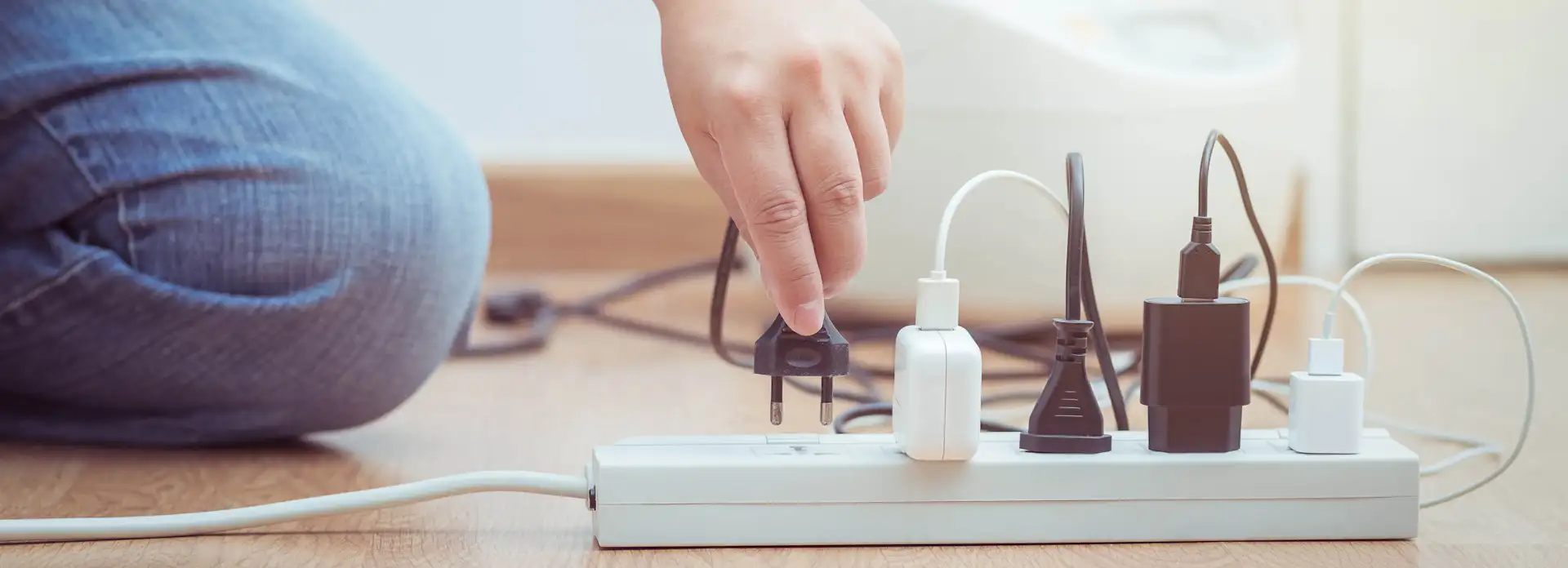Schwarzer Stecker wird in weiße Steckdosenleiste gesteckt Hand Jeans