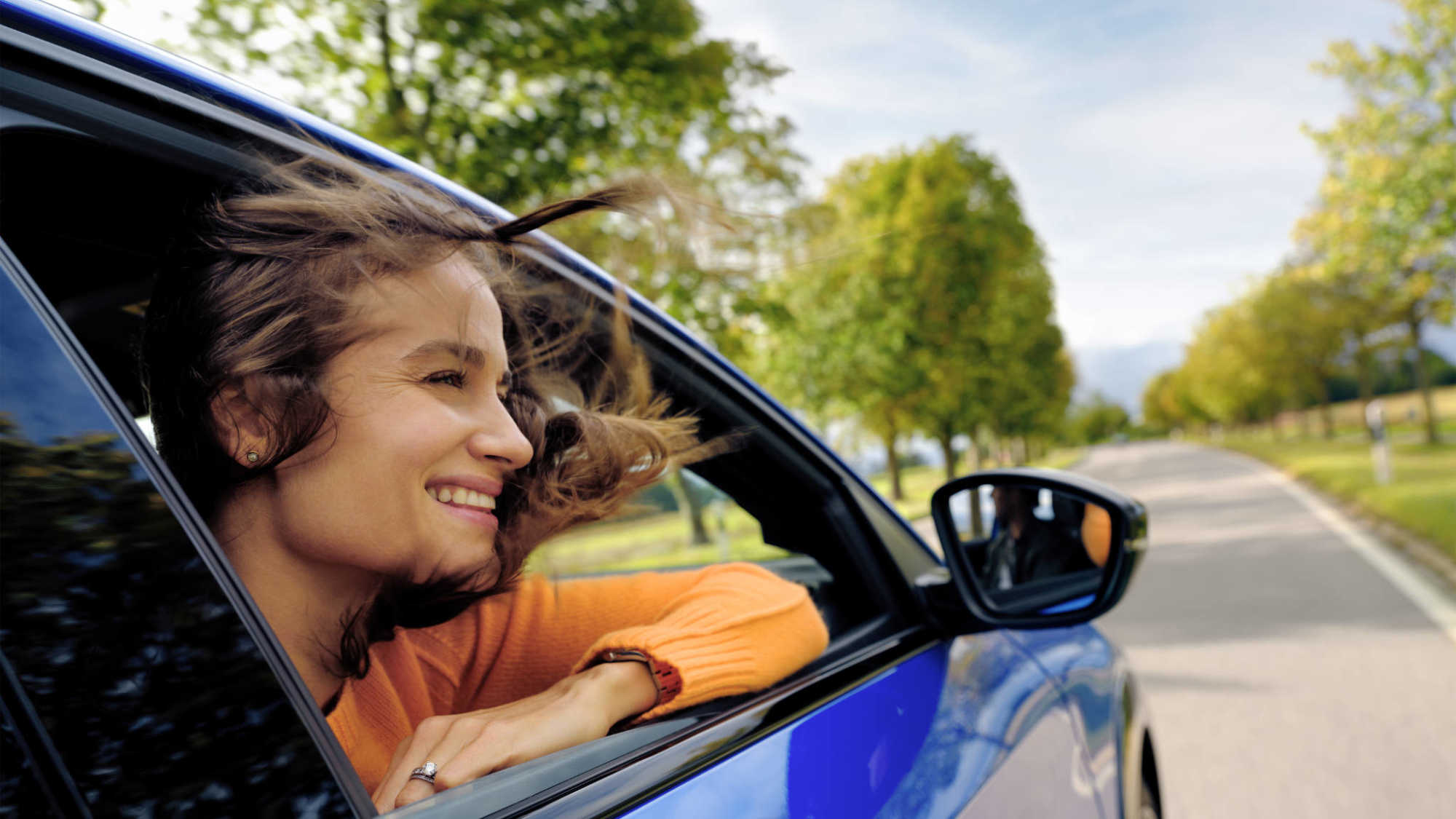 Frau in orangenem Pullover schaut während Fahrt aus blauem E-Auto