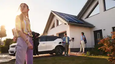 Mädchen mit ihren Eltern vor dem Haus und einem E-Auto, das an der Wallbox Strom vom eigenen Dach lädt