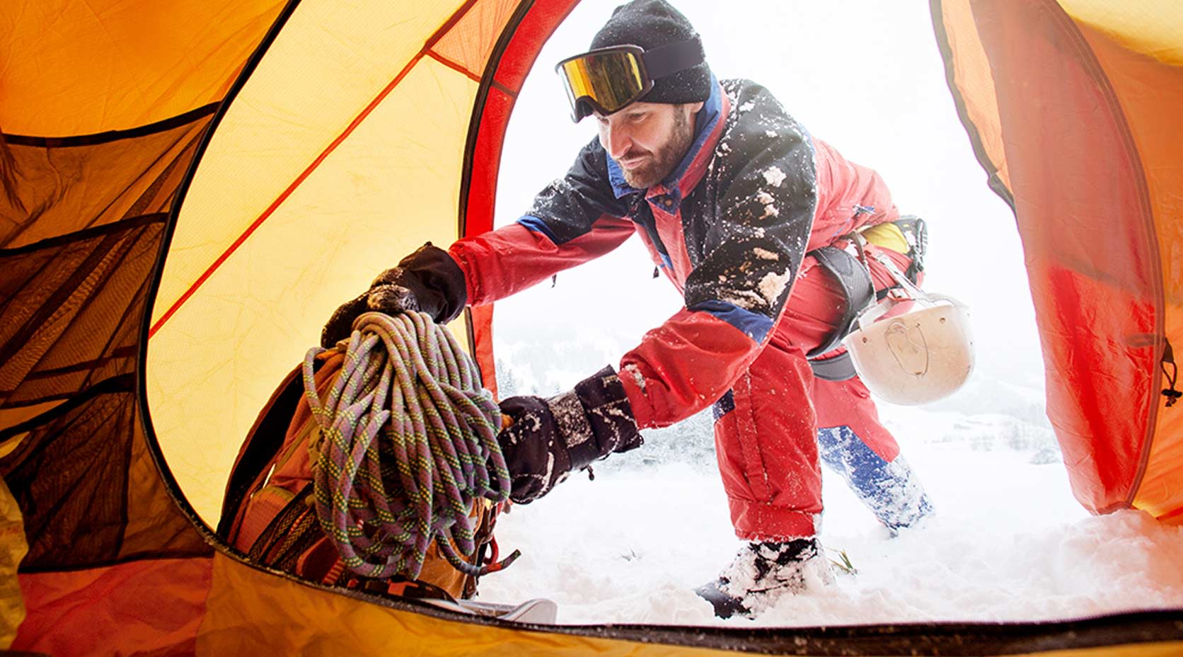 Mann im Schneeanzug holt Ausrüstung aus dem Zelt