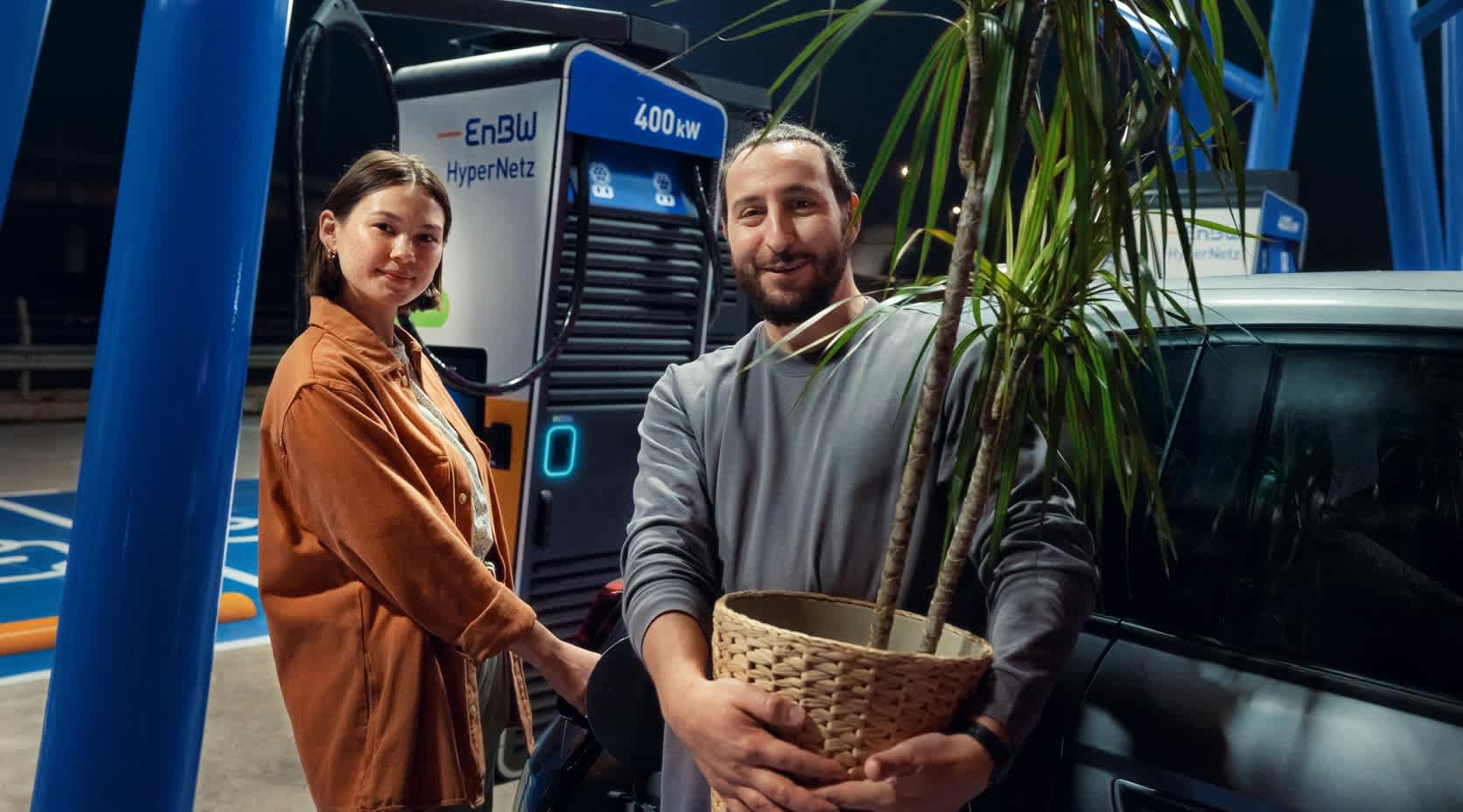 Ein Pärchen mit der Pflanze an einer EnBW Ladesäule.
