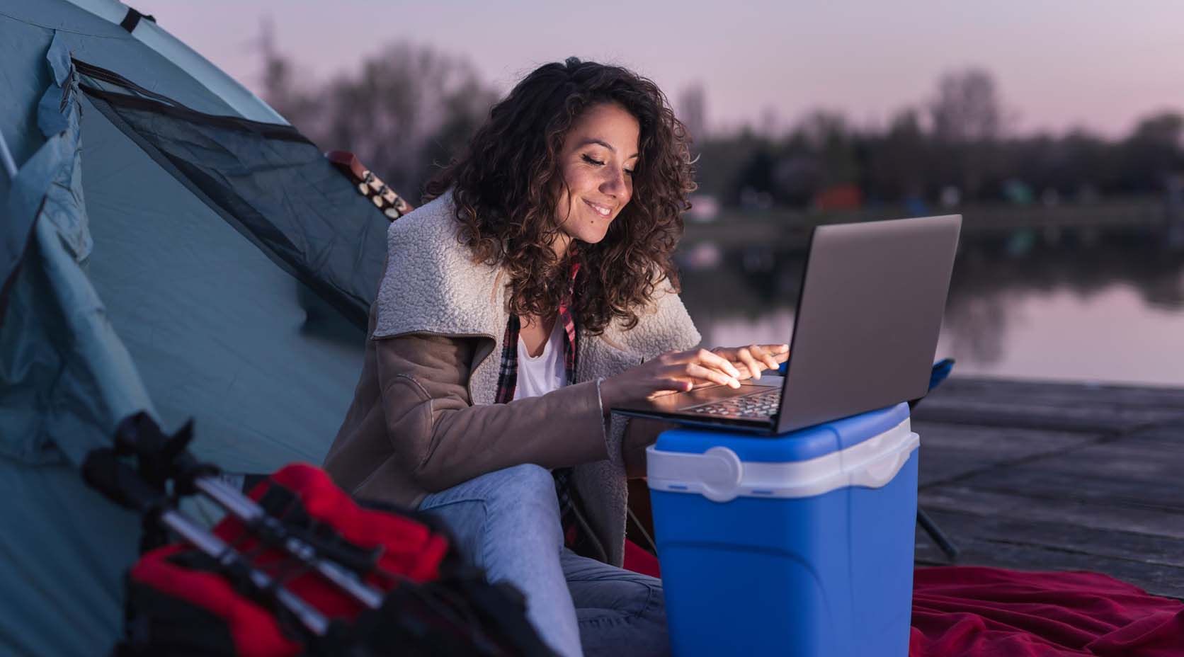 Frau mit Notebook beim Camping an einem See