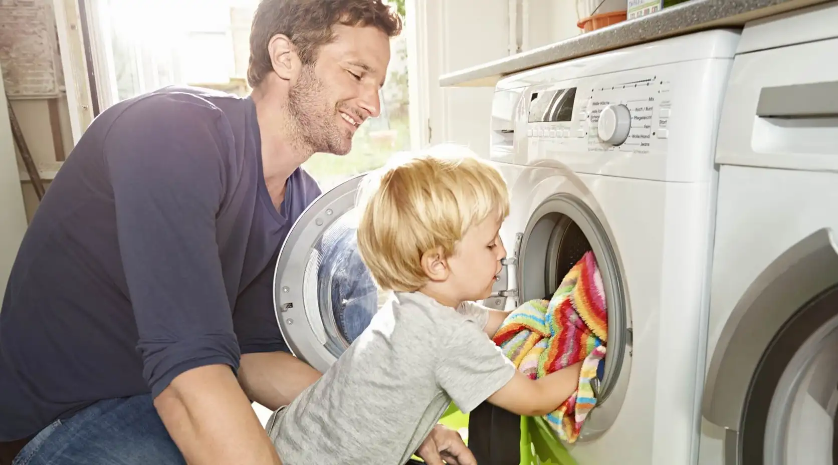 Vater und Kind räumen Waschmaschine ein