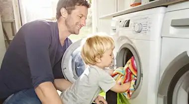 Vater und Kind räumen Waschmaschine ein