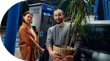 Ein Pärchen lädt an einer EnBW Ladesäule. Der Mann trägt eine Pflanze.