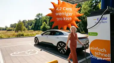 Frau lädt E-Auto an EnBW-Ladestation im EnBW HyperNetz, hinter ihr schwebt ein Luftballon in Form einer Sonne mit der Aufschrift "4,2 Cent weniger pro KWh"